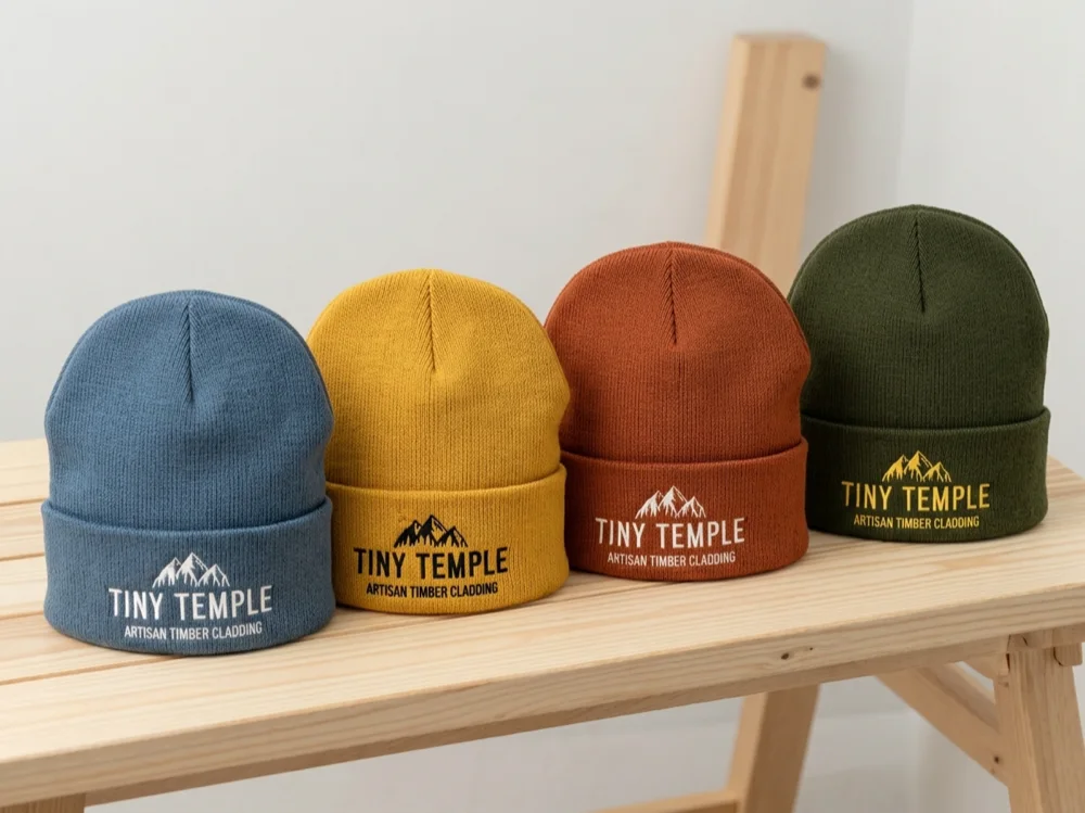 Four knitted Tiny Temple beanies on a pine bench — slate blue, mustard, rust and olive green.