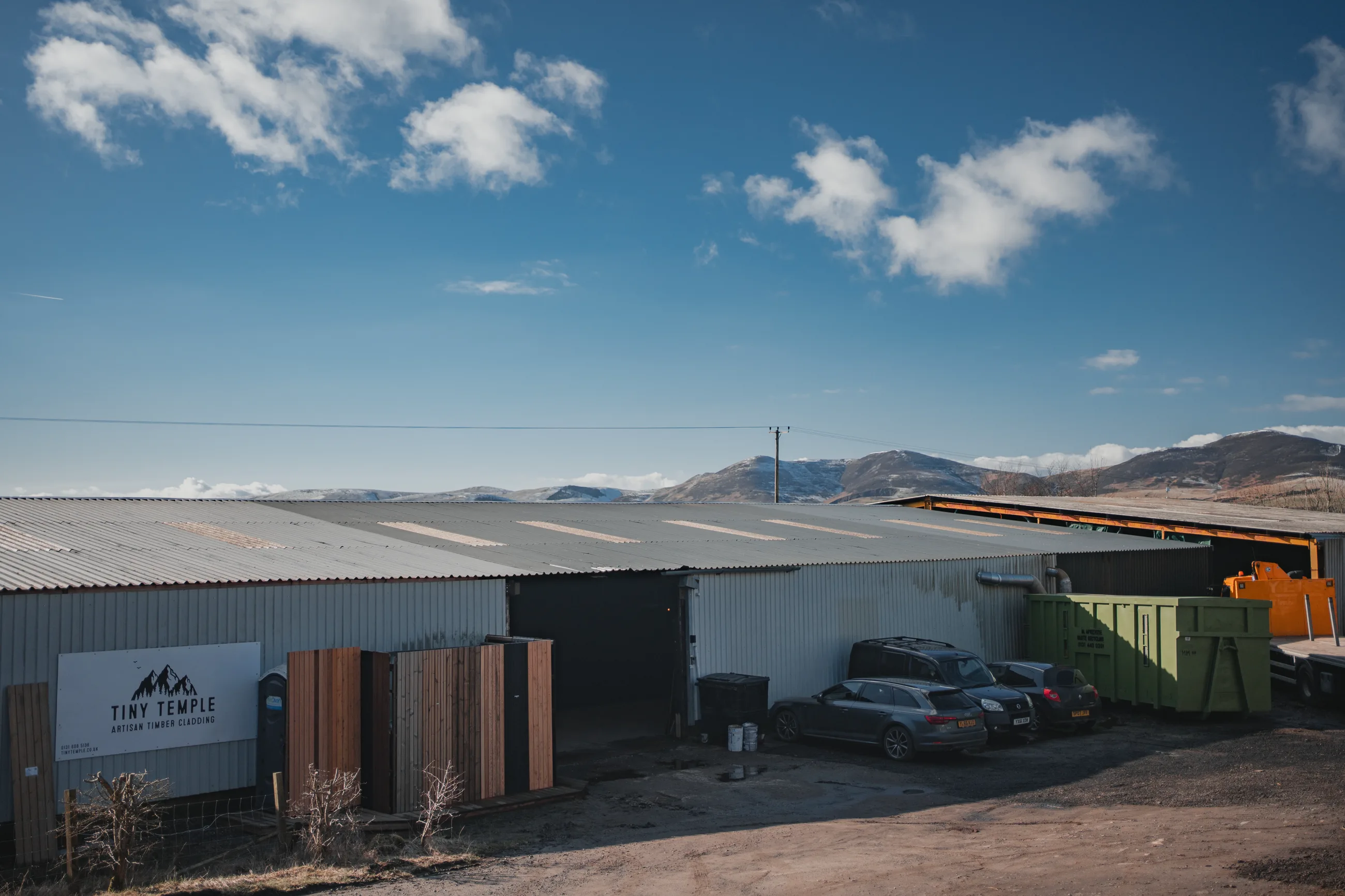 The Tiny Temple mill at Pomathorn Farm — a steel-clad shed with the sign by the door, hills behind.